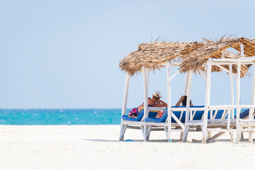 Senior couple relaxing on deck chairs at the beach.White sandy beach and turquoise ocean,luxury...