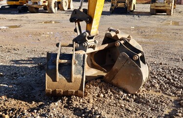 Group of different bucket types under the excavator boom on the ground of a construction site.