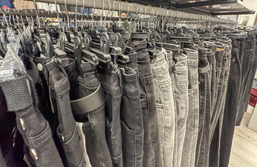 Grey and black jeans on the hangers in the clothes shop. Black denims in the shop. Trousers.