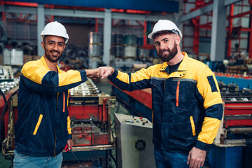 Engineer and industrial worker in uniform shaking hands in large metal factory hall and talking.