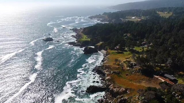 Drone video of the ocean meeting the coastline at Bodega Bay and Gualala Coast, California. View from top perspective, the landscape surrounded by greenery.