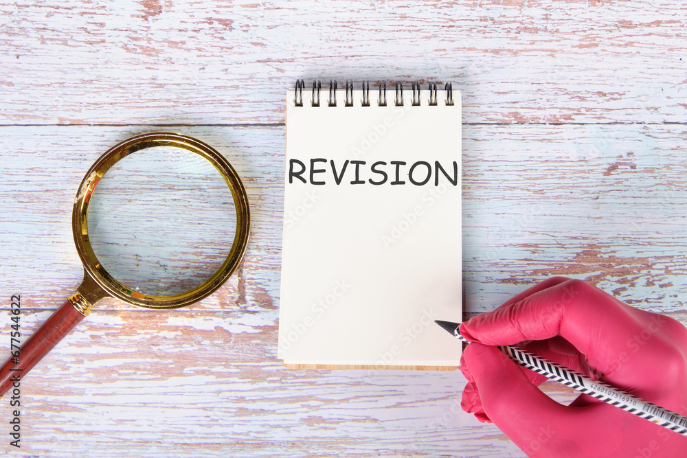 Wall mural REVISION writing on a notebook lying on old boards next to a magnifying glass and a hand in a red medical glove with a pencil