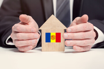 Businessman hand holding wooden home model with Andorran flag. insurance and property concepts