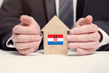 Businessman hand holding wooden home model with Croatian flag. insurance and property concepts