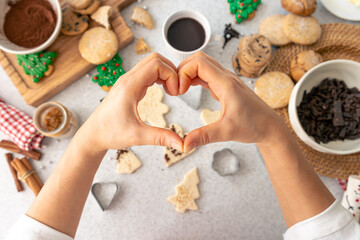 Woman shows a heart with her hands on the background of a table with cookies.