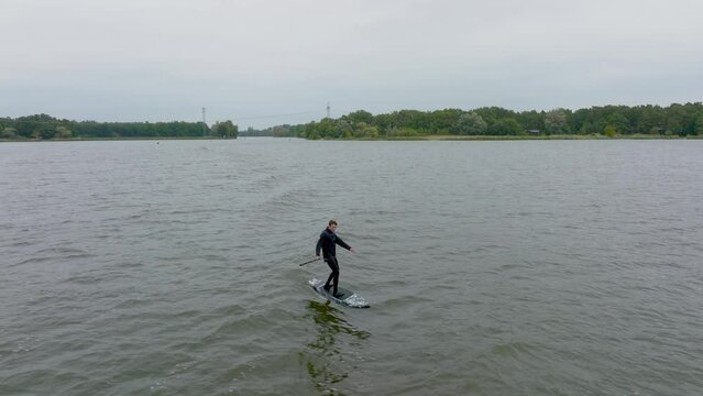 athlete on hydro sup foil surf in wave on a river and fall in water filmed with drone in front of close up
