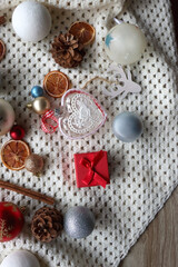 Various colorful Christmas ornaments, small presents and seasonal spices on white knitted blanket. Top view.