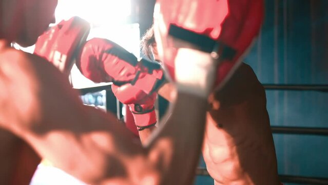 Asian and Caucasian Muay Thai boxer unleash punch in fierce boxing training session, delivering punching strike to sparring trainer, showcasing Muay Thai boxing technique and skill. Impetus