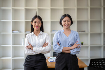 Two smart woman standing with arms crossed in modern office.