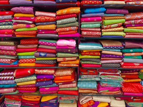 Neatly stacked colorful silk saris in racks in a textile shop, These exquisite, expensive sarees are famous for their gold and silver zari, brocade. Incredible India.