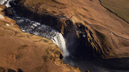 Drone shot of skgafoss waterfall forming beautiful rainbow, icelandic landscape with nordic nature. Spectacular scandinavian cascade flowing down off of cliffs, panoramic view. Slow motion. - obrazy, fototapety, plakaty