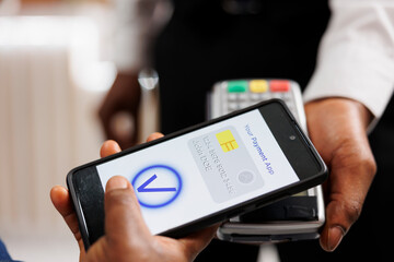 Close up of human hand holding smartphone using mobile nfc payment while paying for hotel services, contactless POS payment. People using banking app to pay via NFC technology, mobile wallet - obrazy, fototapety, plakaty
