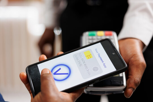 Close up of human hand holding smartphone using mobile nfc payment while paying for hotel services, contactless POS payment. People using banking app to pay via NFC technology, mobile wallet