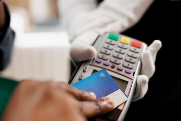 Close up of hotel guest paying for room at front desk, male hand holding plastic credit card making contactless payment. Cashless transactions and nfc technology in hospitality industry
