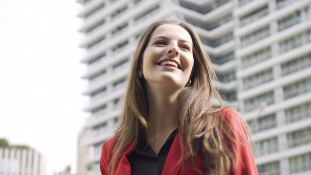 A young beautiful Caucasian businesswoman dances with a smile - closeup - an office building in the blurry building