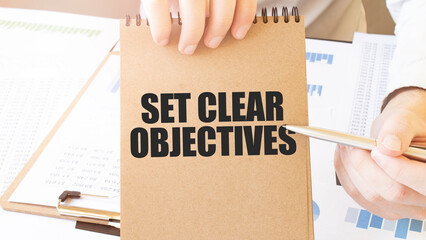 Text SET CLEAR OBJECTIVES on brown paper notepad in businessman hands on the table with diagram....