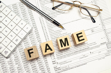 FAME word on wooden blocks with calculator and pen