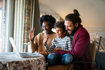 Happy modern multiethnic diverse parents and kid waving hands while using laptop for video chat