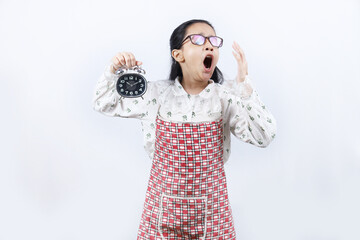 Indian punctual girl holding alarm clock in hand and yawning. teenage girl child wearing apron, standing on white background. 