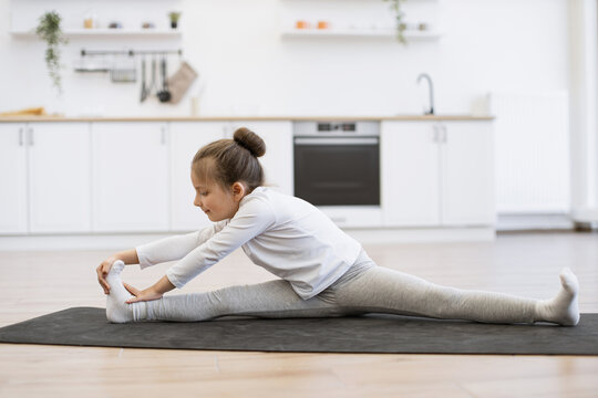 Fitness, little preschool female training yoga in half tortoise pose in kitchen floor at home, copy space. Young slim girl in white sportswear makes stretching training doing splits exercise. - Powered by Adobe