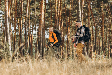 Couple hiking with bags and walking sticks in forest