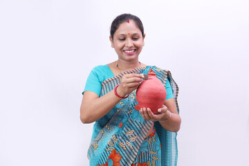 Happy Indian rural woman in saree standing holding a piggy bank in hand cheerfully showcasing various moods of saving money and banking concepts, savings.