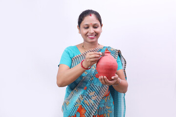 Happy Indian rural woman in saree standing holding a piggy bank in hand cheerfully showcasing...