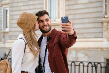 Young Caucasian couple taking a selfie while kissing and sightseeing the city of Madrid, Spain.