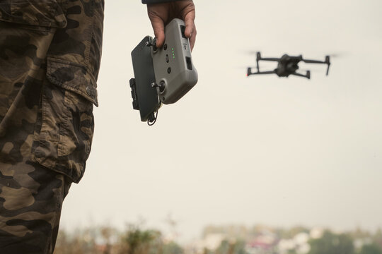 man in a military uniform with a UAV control panel in his hands, a drone flying in the background in nature - Powered by Adobe