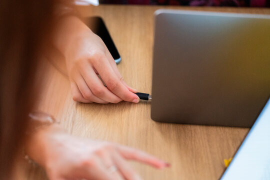 From above of crop anonymous female colleagues plugging USB cord from smartphone to laptop over wooden table while working on project in modern workspace