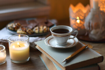 Cup of tea or coffee, plate with desserts, dried oranges, bowl of grapes, scented candles, vintage books, pumpkins and autumn leaves on the table. Autumnal hygge. Selective focus.