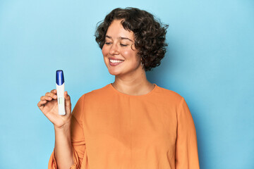 Young Caucasian woman holding a pregnancy test, studio blue background.
