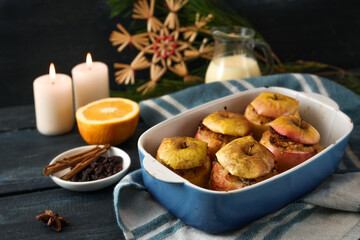 German baked apples filled with almonds, marzipan and honey in a casserole, ingredients, candles, and Christmas decoration against a dark blue background, festive holiday dessert, selected focus
