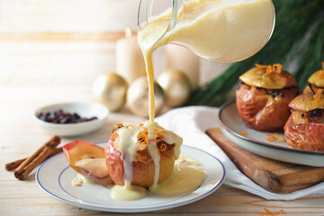 Pouring vanilla sauce on a baked apple filled with almonds, honey and raisins, homemade winter...
