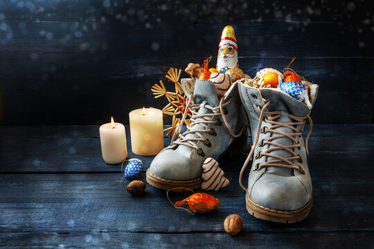 Tradition on German Nikolaus Tag meaning Nicholas day, shoes are filled with treats, here boots with sweets and Christmas decoration on dark blue wood with candles, copy space