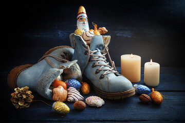 Blue boots filled with sweets, Christmas decoration and a chocolate Santa on dark wood with candles, tradition on German Nikolaus Tag meaning Nicholas day at 6th December, copy space