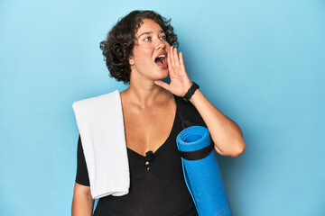 Athletic young woman with yoga mat shouting and holding palm near opened mouth.