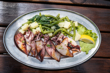Grilled baby squids on a plate with mashed potatoes and spinach garnish served in a traditional seafood restaurant in Montenegro. Grilled calamari on a table.