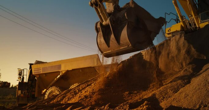 Construction Site On Sunny Evening: Industrial Excavator Loading Sand Into A Truck. The Process Of Building New Apartment Complex. Workers Operating Heavy Machinery To Complete A Real Estate Project.