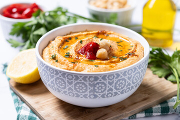 Roasted red pepper hummus in white bowl on white marble background.