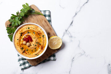 Roasted red pepper hummus in white bowl on white marble background. Top view. Copy space