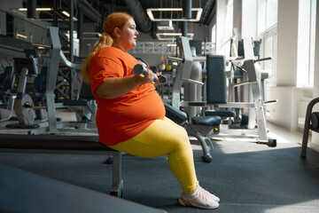 Plus size woman doing exercise on biceps training with dumbbells at gym