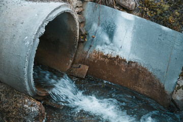 Wastewater and sewage flow from a pipe into a polluted river, creating a bad smell and a chemical...