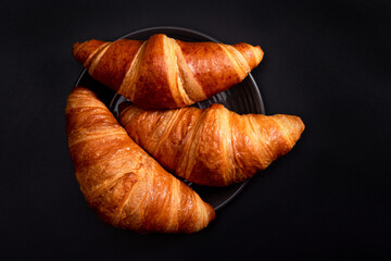 Freshly baked croissants in a black plate on a dark black background. Croissant cooking concept.