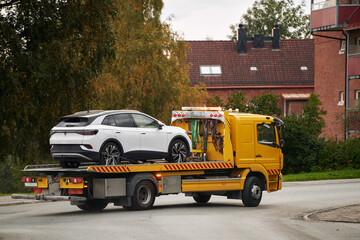 A tow truck carries a car on a flatbed trailer on the highway, providing transport service and...