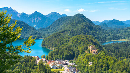 Aerial view  of a mountain valley in south Bavaria, Germany, with the famous medieval castle named "Hohenschwangau" visible on the right. Lakes with blue waters at both sides.