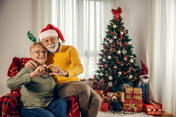 Obraz na płótnie Canvas Grandparents making heart shape gesture while sitting at home on christmas and new year.
