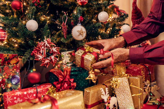 Cropped picture of senior man's hands putting gift under the christmas tree on christmas and new year.
