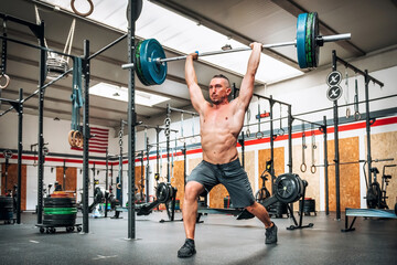 Muscular sportsman lifting barbell in modern gym