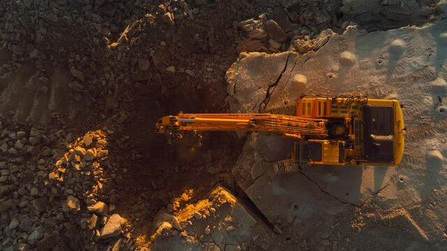 Aerial Drone Shot Directly Above Industrial Excavator Digging Up Rocks On Construction Site On Sunny Day. Workers Operating Heavy Machinery To Complete Real Estate Project Or Extract Natural Resources